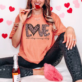 Love All Day Every Day Faux Glitter Leopard DTF Heat Transfer, a woman in casual pajamas with leopard print leggings and a pink script T-shirt with the word LOVE filled with leopard print, sitting on a white fluffy surface, surrounded by pink and red paper hearts, holding a lollipop and a bottle of rosé, in a Valentine's Day themed setting.