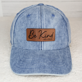 Be Kind... of a bitch Leather Hat Patch, blue denim baseball cap with a brown leather patch that has the text 'Be Kind... of a bitch' embroidered on it.