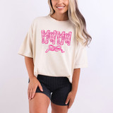 Mama Patterned DTF Heat Transfer, pink and white patterned text with bow design on a white t-shirt worn by a smiling woman.