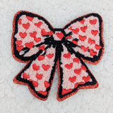 Chenille Bow With Embroidered Hearts HAT/POCKET Patch, a decorative patch featuring a pink chenille bow with red embroidered hearts and black outlines, enhanced with red glitter edging.
