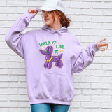 Walk It Like A Dog DTF Heat Transfer, a colorful design of a balloon dog wearing a green nose and yellow beads, with the text 'Walk It Like A' in green, on a woman wearing a lavender hoodie.