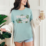 Plant Lady Boho DTF Heat Transfer, woman wearing a light blue t-shirt with botanical cactus and succulent design and pink lettering, holding a smoothie in a glass, casual indoor setting.