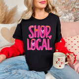 Painted Shop Local DTF Heat Transfer, a colorful pink and purple graphic design with hearts on a black t-shirt worn by a person sitting on a cozy couch.