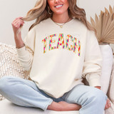 Teach Bright Brushstroke DTF Heat Transfer, colorful and vibrant lettering design on a cream sweatshirt worn by a smiling woman.
