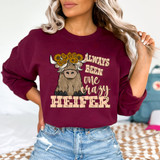 Always Been One Crazy Heifer DTF Heat Transfer, humorous cow graphic with sunflower crown and playful text on a woman's maroon sweatshirt.