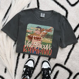 The Great Bambino DTF Heat Transfer, a colorful graphic t-shirt with football-themed text and images, laid flat on a patterned rug with sneakers below.