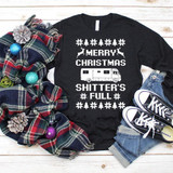 Merry Christmas Shitter's Full Christmas Vacation Screen Print Transfer, black long sleeve shirt with holiday-themed graphics and text, surrounded by holiday decorations and casual accessories.