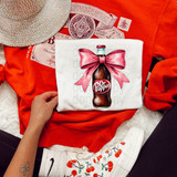 DrP Coquette DTF Heat Transfer, vibrant printed design of a bottle of Dr. Pepper with a pink bow on a white fabric.
