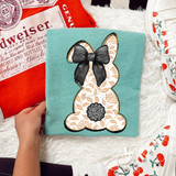Tan Pattern Bunny DTF Heat Transfer, a fabric featuring a bunny design with a black bow and floral pattern on beige, set against a turquoise background.