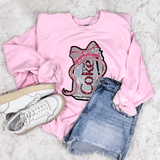 Diet Coke Sequins Patch, pink sweatshirt with sequin patch of a Diet Coke bottle with bow and text, paired with denim shorts and white sneakers
