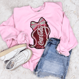 Coke Sequins Patch, pink sweatshirt with Coca-Cola logo sequin patch, casual denim shorts, and white sneakers laid out on a textured surface.