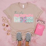 The Lord Is My Shepherd Floral DTF Heat Transfer, beige T-shirt with colorful floral design and scripture Psalm 23, placed on pink fluffy surface with gold rings, a pink Bible, and checkered slip-on shoes.