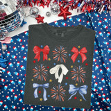 Coquette Fireworks DTF Heat Transfer, a graphic design of colorful bows and fireworks on a dark gray t-shirt, surrounded by festive decorations in the image.