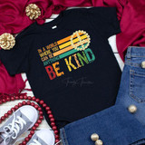 In a World Where You Can Be Anything Be Kind Youth Screen Print Heat Transfer T-shirt, black T-shirt with colorful 'Be Kind' design, surrounded by jeans, sneakers, red and gold decorations.
