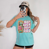 Not Luck Just God Faux Glitter DTF Heat Transfer, image of a woman wearing a light blue T-shirt with a colorful graphic print and text, taking a mirror selfie with her smartphone.