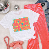 Jesus Loves You & I'm Trying Colorful Retro DTF Heat Transfer on a white T-shirt with a vibrant, psychedelic font, laid out alongside pink velvet pants, denim jacket, disco balls, and a pink rotary phone, creating a stylish and colorful fashion display.