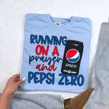 Running On A Prayer And Pep Zero DTF Heat Transfer, a light blue t-shirt with a humorous graphic design featuring a soda can and the text 'Running On A Prayer and Pep Zero' for customized apparel printing.
