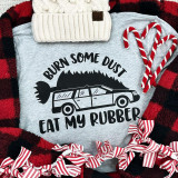 Burn Some Dust Eat My Rubber Christmas Vacation Screen Print Transfer, a humorous Christmas-themed graphic featuring a car with a Christmas tree on top and the phrase 'Burn Some Dust Eat My Rubber' in black text on a grey fabric background.