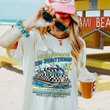 High Noons On Pontoons DTF Heat Transfer, a woman holding sunglasses and a drink at the beach wearing a T-shirt with a boat and wave design.