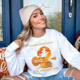 Dark Desert Highway Witch Screen Print Heat Transfer, woman wearing a white sweatshirt with a witch flying on a broomstick in front of a full moon over a lake, with orange trees, and the text 'On a Dark Desert Highway, Cool Wind in My Hair'.