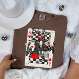 Baby I'm a Wildcard DTF Heat Transfer, graphic design with playing cards, lipstick lips, cherries, dice, and a soda can, on a brown t-shirt.