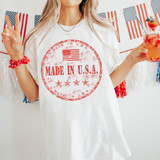 Made In The USA RED DTF Heat Transfer, a woman wearing a white T-shirt with a red distressed 'Made In U.S.A.' stamp design, celebrating American pride with festive decorations in the background.