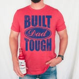 Built Dad Tough DTF Heat Transfer, a graphic design on a red T-shirt featuring bold blue text and a distressed finish.