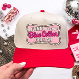 Living On That Blue Collar Dollar DTF Heat Transfer, a baseball cap with a white front panel and red brim and button, featuring bold pink and black text design.