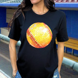 Glitz Softball DTF Heat Transfer, sparkling yellow-orange softball with red stitches on a black t-shirt worn by a woman.