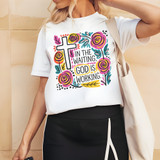 In The Waiting God Is Working Boho DTF Heat Transfer, colorful floral and religious design on a white T-shirt worn by a woman.