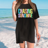 Distressed Colorful Chasing Sunshine DTF Heat Transfer, colorful distressed text design on black T-shirt worn by woman at the beach.