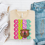 Stacked Retro Mascot DTF Heat Transfer, colorful graphic design with a bear and the word 'CUBS' repeated in pink, green, and purple, on a beige T-shirt laid flat with blue jeans, white sneakers, and jewelry around it.