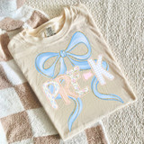 Pastel Bow Back To School DTF Heat Transfer, image of a beige T-shirt featuring a large pastel blue bow and the phrase 'PEEK' in colorful, patterned letters.