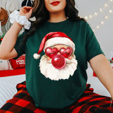 Faux Glitter Bubblegum Santa with Heart Glasses DTF Heat Transfer, festive holiday Christmas design on a woman's dark green shirt, featuring Santa with glittery red nose, heart-shaped sunglasses, and a Santa hat.