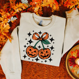 Pumpkin Cherries DTF Heat Transfer, Halloween-themed sweatshirt with illustrated carved pumpkins with bow and surrounding stars on autumn leaves background.