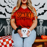 Spooky Season Ghost Script DTF Heat Transfer, a Halloween-themed t-shirt with ghost design and text, worn by a woman sitting with Halloween decorations.
