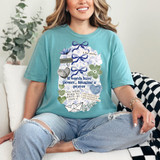 If Words Have Power, Imagine A Prayer DTF Heat Transfer, a woman wearing a turquoise t-shirt with inspirational words and floral designs, sitting on a sofa with a cheerful smile.