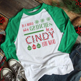 In a World Full Screen Print Heat Transfer, holiday-themed Christmas T-shirt with green and red text and ornaments on a white and green baseball tee