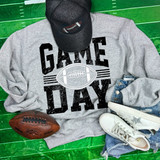 Game Day Various Colors/Puff Ink Screen Print, grey sweatshirt with black and white football design and text, paired with white sneakers, denim shorts, a black cap with glitter, and an American football on a green surface.