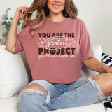 You Are The Greatest Project DTF Heat Transfer, a woman wearing a casual pink T-shirt with the motivational quote, sitting on a white couch.