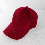 Cranberry Corduroy Hat, a red corduroy baseball cap with a curved brim and button top, placed on a soft white surface.