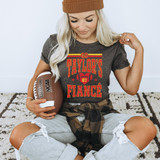 Go Taylor's Fiance DTF Heat Transfer, woman wearing a dark t-shirt with red and yellow design, sitting on the carpet, holding a football.