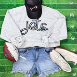 Jets Sequin Patch, casual sports-themed outfit with grey sweatshirt, distressed denim shorts, white sneakers, black cap with football logo, and football placed on a green measuring tape background.