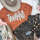 Double Layer Stacked Thankful Fluffy Patch, fashion outfit with a rust-colored T-shirt with 'thankful' in white embroidered letters, leopard print pants, gold sneakers, a beige sunhat, and a beaded necklace.