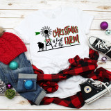 Christmas is Best at the Farm Windmill Cow Sublimation Transfer, white T-shirt with farm and Christmas themed design, surrounded by jeans, plaid shirt, sneakers, and Christmas ornaments on a wooden background.