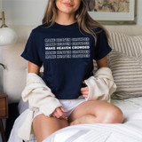 Make Heaven Crowded Stacked WHITE DTF Heat Transfer, a person wearing a navy blue T-shirt with the repeated text 'MAKE HEAVEN CROWDED' in white with black outlines, sitting on a bed with striped pillows and a cozy cardigan.