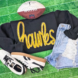 Gold Hawks Sequin Patch, a black sweatshirt with yellow sequined 'thanks' lettering, paired with distressed denim shorts, white Reebok sneakers, and a football on a green turf background.