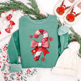 Patchwork Candy Cane DTF Heat Transfer, Christmas-themed cotton sweatshirt with candy cane design made of patchwork fabric with red and white stripes, polka dots, and snowflake accents, surrounded by holiday decorations including reindeer slippers, knitted hat, greenery, and ornaments.