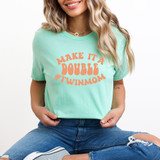 Make It A Double #TwinMom DTF Heat Transfer, a woman wearing a mint green t-shirt with orange text that says 'Make It A Double #TwinMom'.