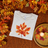Painted Maple Leaf DTF Heat Transfer, an orange-red painted maple leaf design on a white t-shirt, surrounded by fall leaves and a lit candle on a wooden tray.